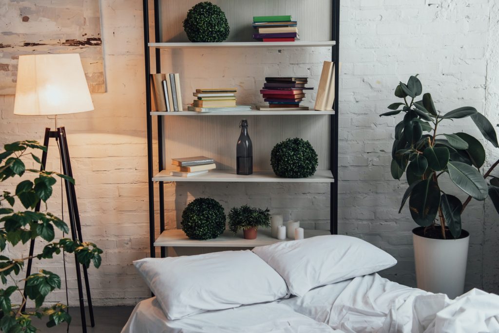 modern interior design of bedroom with rack, plants, lamp, bed and brick wall