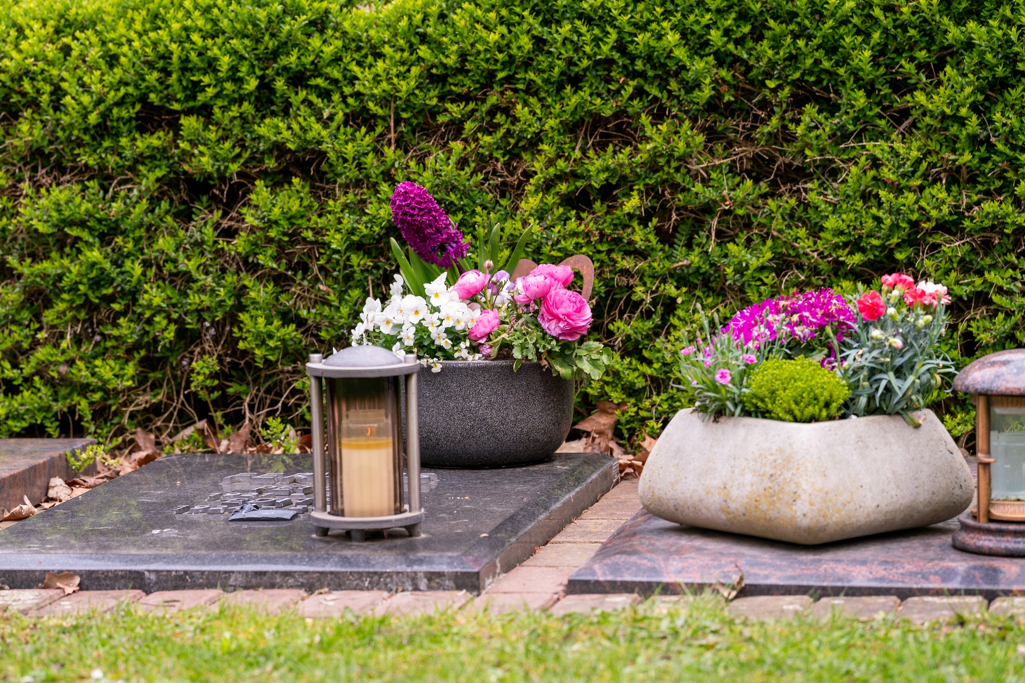 Grave light with burning candle on a grave with flowers