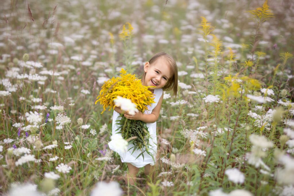 Girl with a bouquet of goldenrod flowers in a large field of blooming achillea millefolium