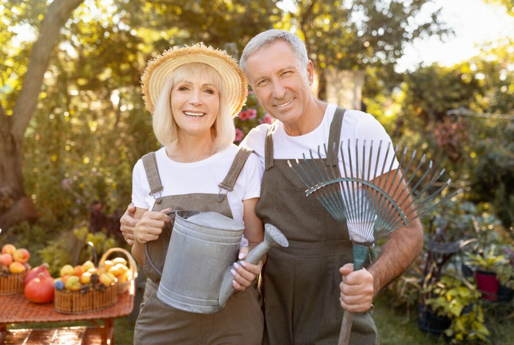 Lovely senior spouses holding gardening tools, working in garden at sunny day