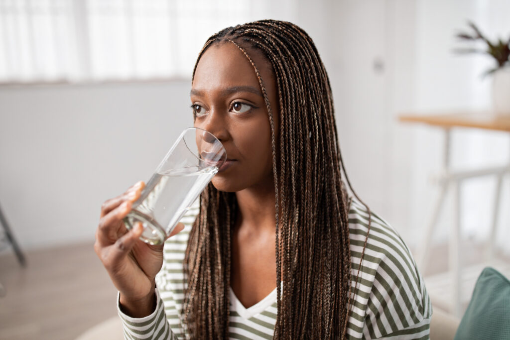 Closeup of young black woman drinking water at home