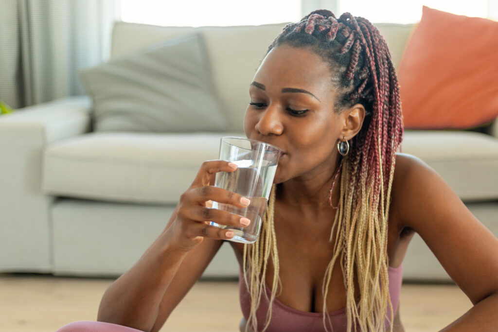 Domestic sports and hydration. Young african american woman drinking fresh water from glass, resting