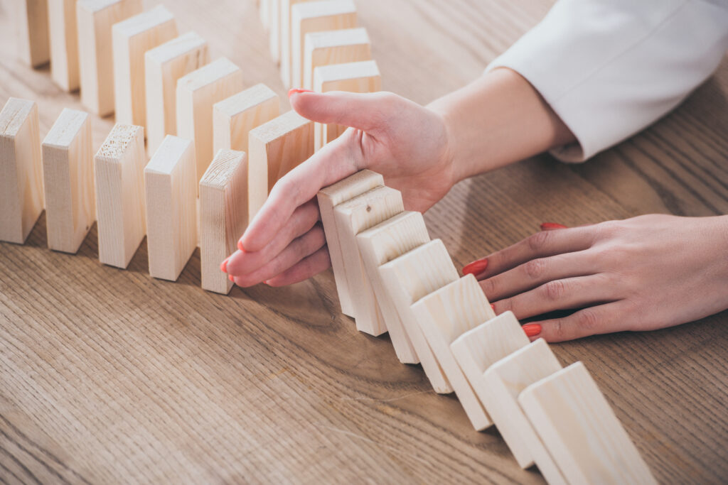 partial view of risk manager blocking domino effect of falling wooden blocks