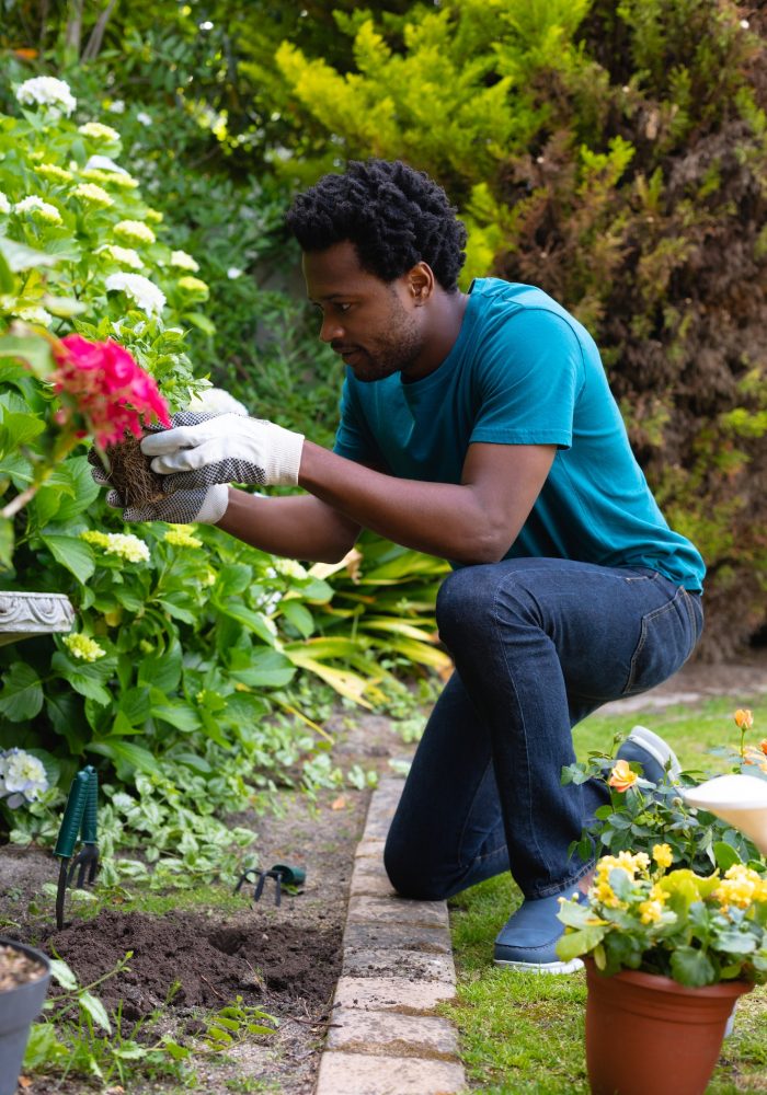 Full length of young african american man kneeling while gardening in backyard