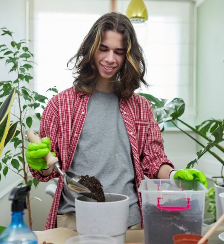 Guy teenager caring replanting indoor plants in pots